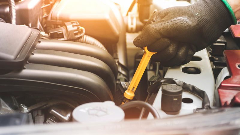 Gloved technician checking a vehicle's engine oil level with a dipstick